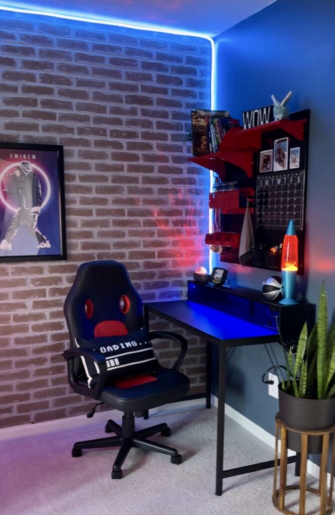 Faux brick wall backlit by neon lights. In front of the wall, is a gamer chair and desk. A modern take on a gamer room used to show the finished product. lakeandlumber.com 