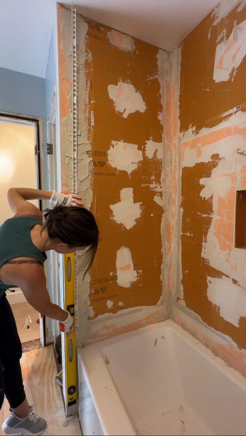 Melissa Tyler using her level to install the Kerdi board egde pieces on the waterproofed shower with visible white patches from the silicone patches. 