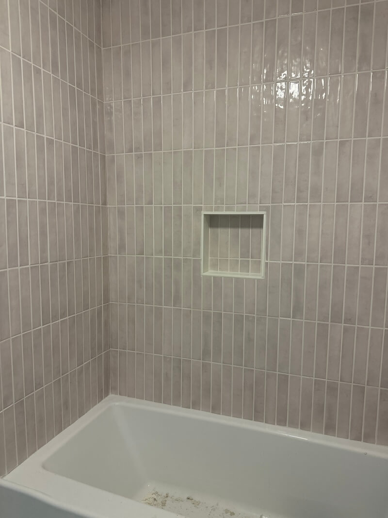 Final reveal of the shower with pink blush tile, white tub, and white marble shower niche. 