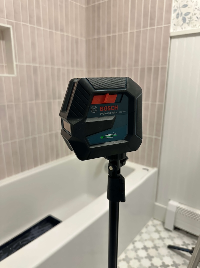 Laser level on a tripod in front of a bathroom shower. 