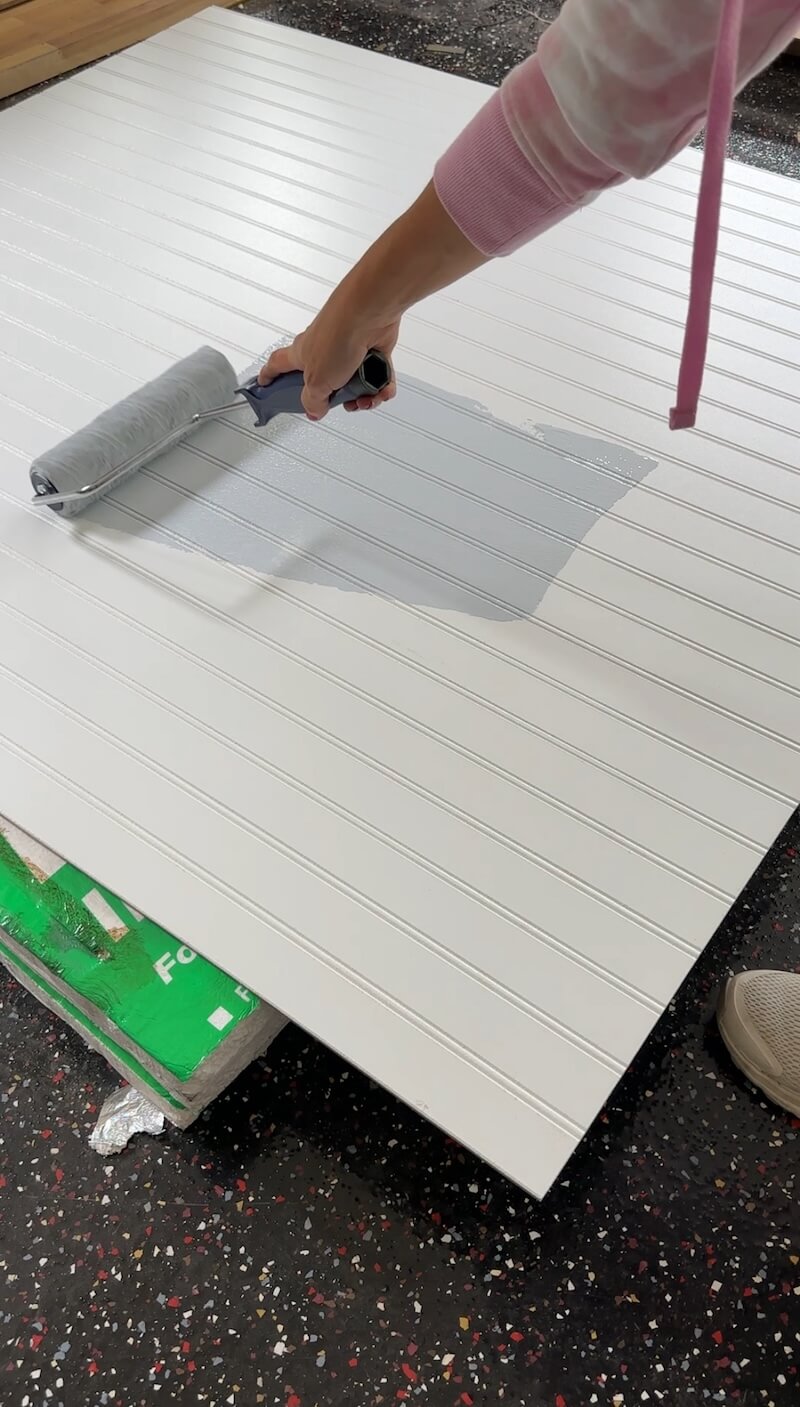 A close up image of a woman starting to paint the white primed MDF beadboard light blue using a foam roller. 