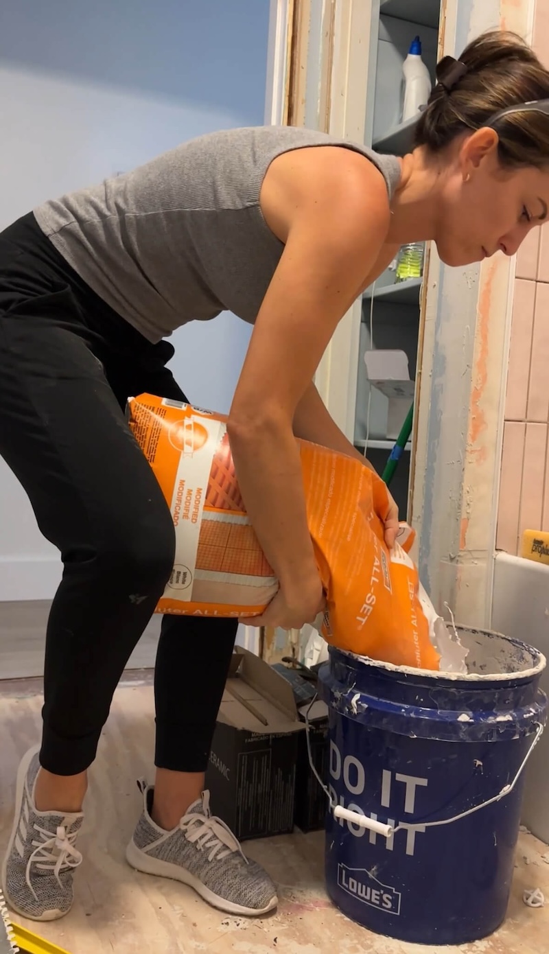 Melissa Tyler mixing thinset by pouring a bag of thinset into a 5-gallon bucket. 