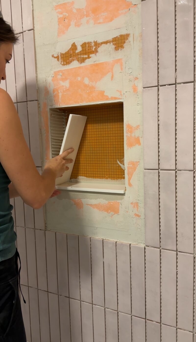 Melissa Tyler putting the first white marble tile in the shower niche. 