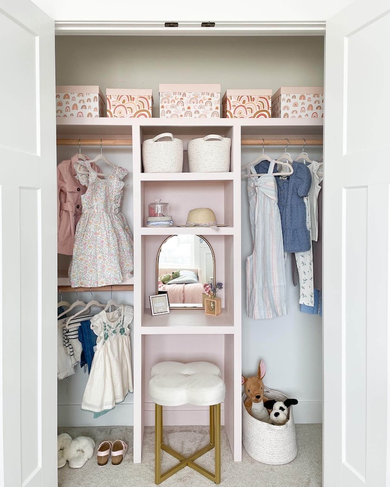 Closet doors open showcasing the finished DIY closet with hanging dresses, pink bins, and a small vanity. 