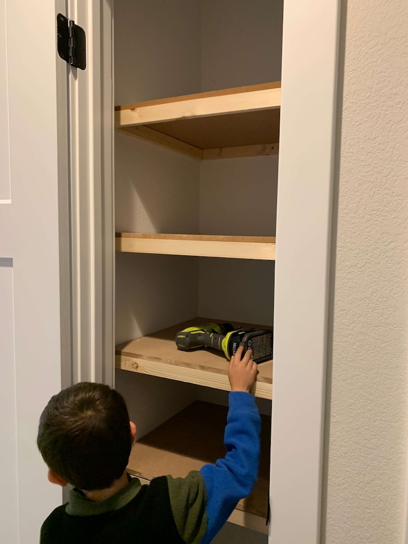 Young boy standing in front of unfinished DIY closet shelves.