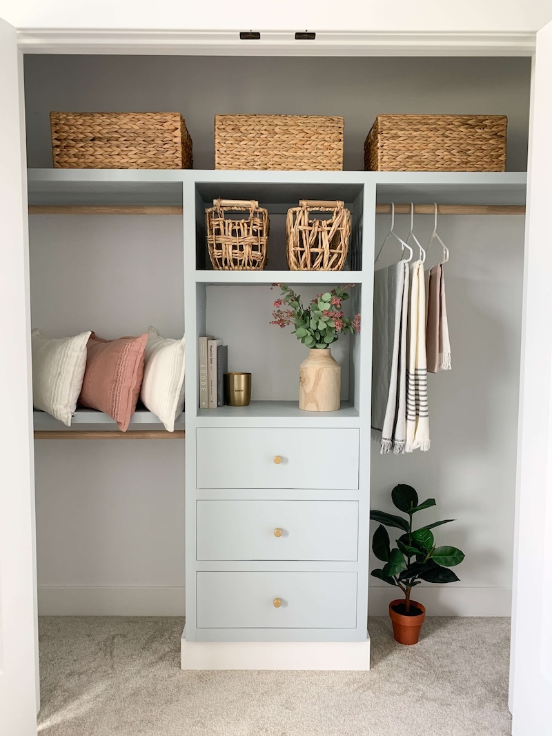 Light blue painted DIY custom closet filled with bins, pillows, and home decor. 