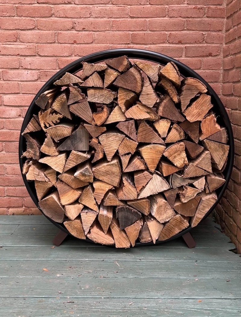 Completed DIY firewood rack full of wood against a brick wall. 