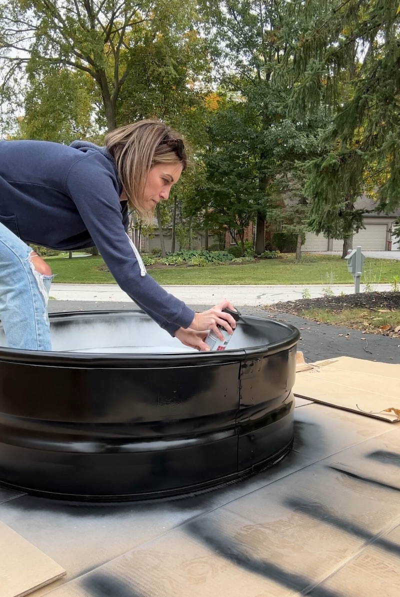 Melissa Tyler painting a metal firewood rack with black Rustoleum spray paint. 