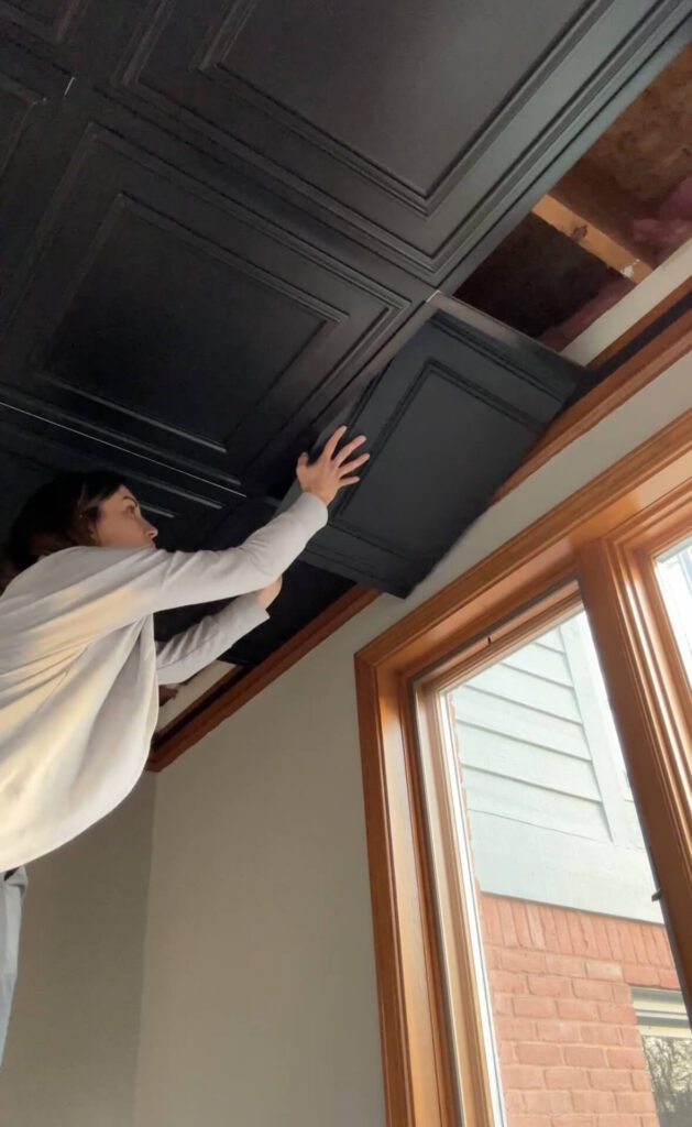 Melissa Tyler popping in a cut tile into her basement drop ceiling.