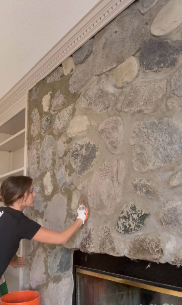 Melissa Tyler applying mortar to her fireplace stones with gloved hands. 